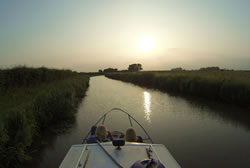 Photo of the front of a canal boat in the Ashby Canal near sunset with fields on either side