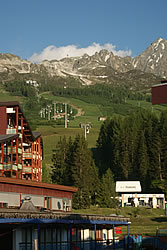 Image of Arc 1800 with a green slope up to the snow of the mountain behind